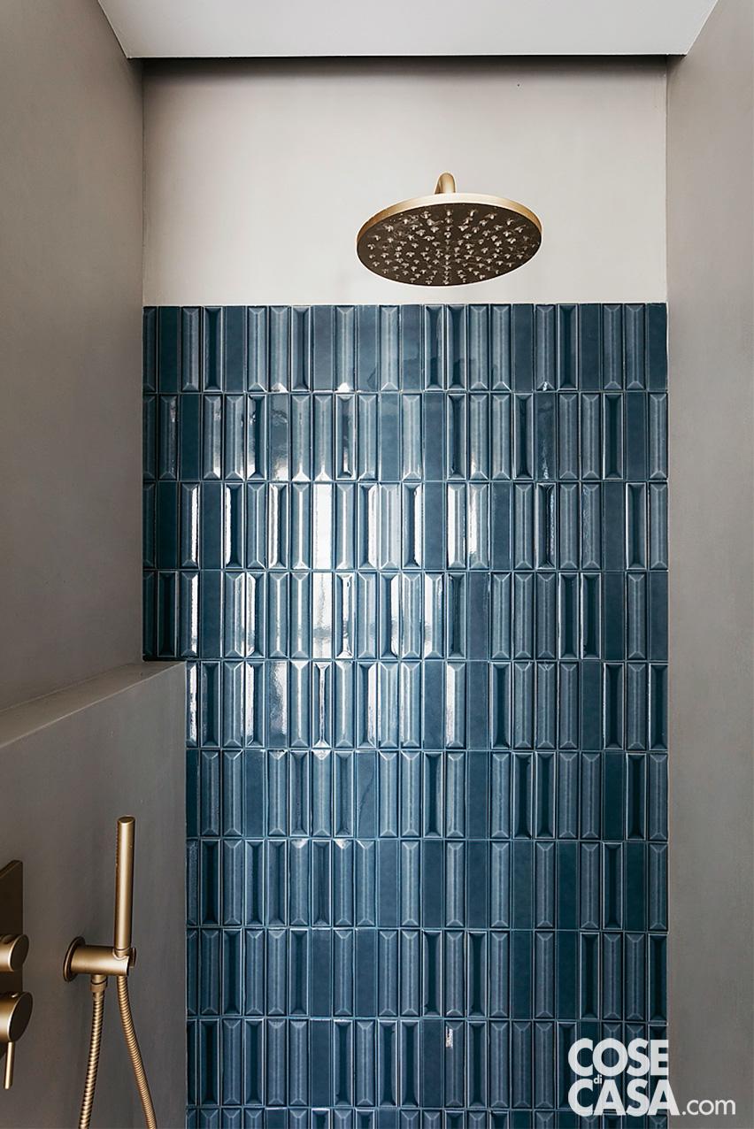 Il bagno è uno degli ambienti in cui il blu navy è più spesso utilizzato, soprattutto per i rivestimenti. In questo caso l’area doccia è delimitata da mattoncini lucidi, che giocano con la luce esterna, e contrastano nobilmente con la rubinetteria dorata e minimale.