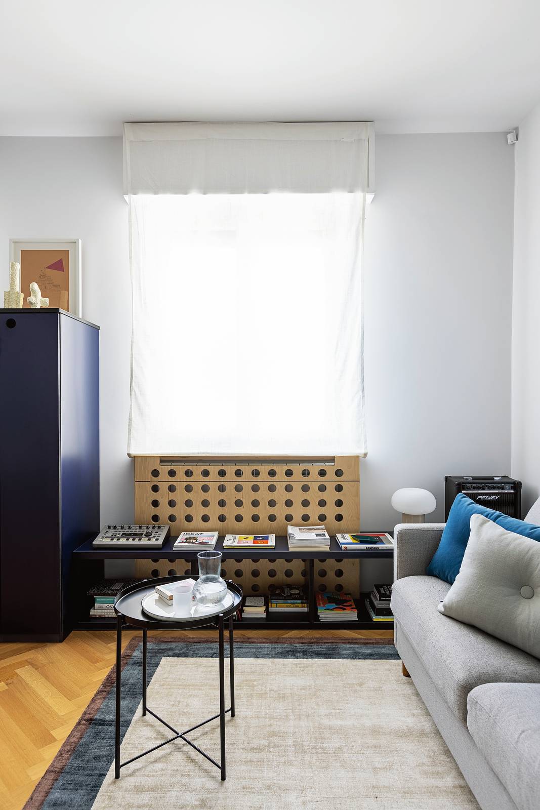 Sotto la finestra, davanti al copriradiatore in Mdf, realizzato su misura con un design traforato sul frontale, è collocata una panca multifunzione con due ripiani: è un elemento versatile che funge da libreria e pratico supporto per una lampada e altro accanto al divano, ma all’occorrenza si trasforma in una seduta aggiuntiva. Foto di Cristina Galliena Bohman Sotto la finestra, davanti al copriradiatore in Mdf, realizzato su misura con un design traforato sul frontale, è collocata una panca multifunzione con due ripiani: è un elemento versatile che funge da libreria e pratico supporto per una lampada e altro accanto al divano, ma all’occorrenza si trasforma in una seduta aggiuntiva. Foto di Cristina Galliena Bohman