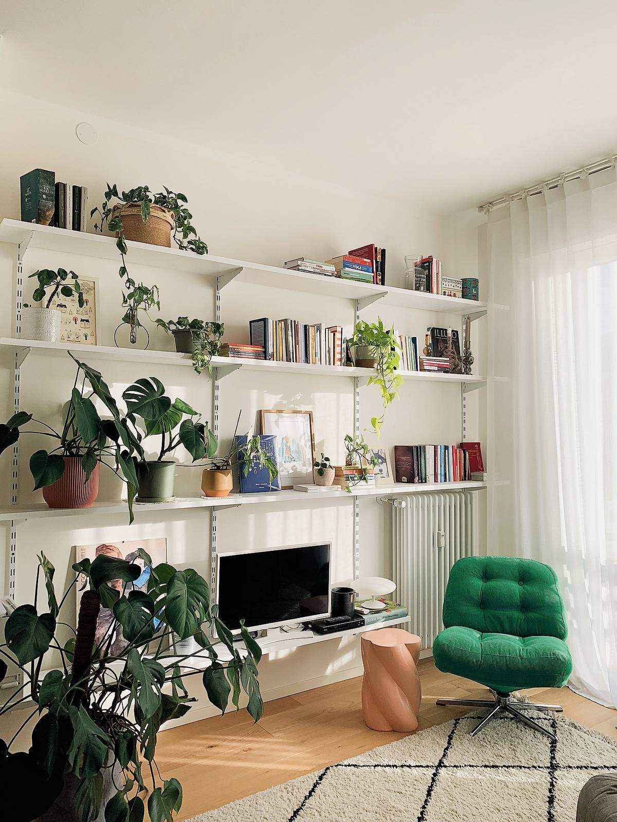 DOPO: La zona conversazione, illuminata dalla luce naturale che filtra dalla finestra sul balcone, trasmette un mood fresco. Le pareti, in un bianco caldo, fanno da sfondo a una libreria a giorno essenziale, che lascia spazio a un angolo lettura. Di fronte, c'è un divano grigio chiaro.