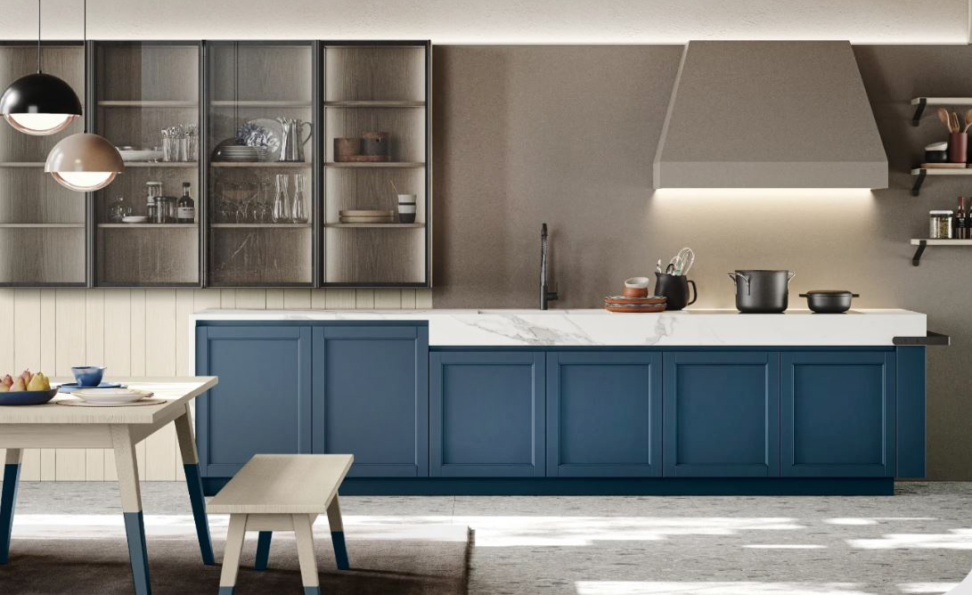 Ha le ante modanate in legno nella finitura blu denim la cucina Maestrale di Scandola Mobili che si sviluppa linearmente lungo la parete. I pensili con il telaio in alluminio, la grande cappa a trapezio e il top in HPL effetto marmo completano la composizione dal sapore elegantemente classico. Prezzo su richiesta. https://www.scandolamobili.it