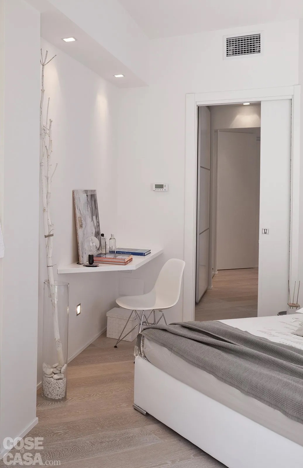 In questa camera da letto dal perimetro irregolare con pareti non perpendicolari, il letto risulta posto in diagonale rispetto alla porta d'ingresso della stanza, realizzata a scomparsa interno muro per annullare l'ingombro. Ne deriva che l'angolo a ridosso della porta non potrebbe ospitare un mobile per via dello scarso spazio antistante che non permetterebbe il passaggio o l'apertura di ante e cassetti. L'idea intelligente e molto pratica è stata quella di utilizzare questo piccolo spazio per posizionare un ripiano sagomato su misura che funge da zona studio con una sedia, il tutto total white per ridurre ulteriormente l'impatto visivo e uniformarlo con porta e pareti.
Progetto arch. Rosy Rozza - Foto Cristina Fiorentini