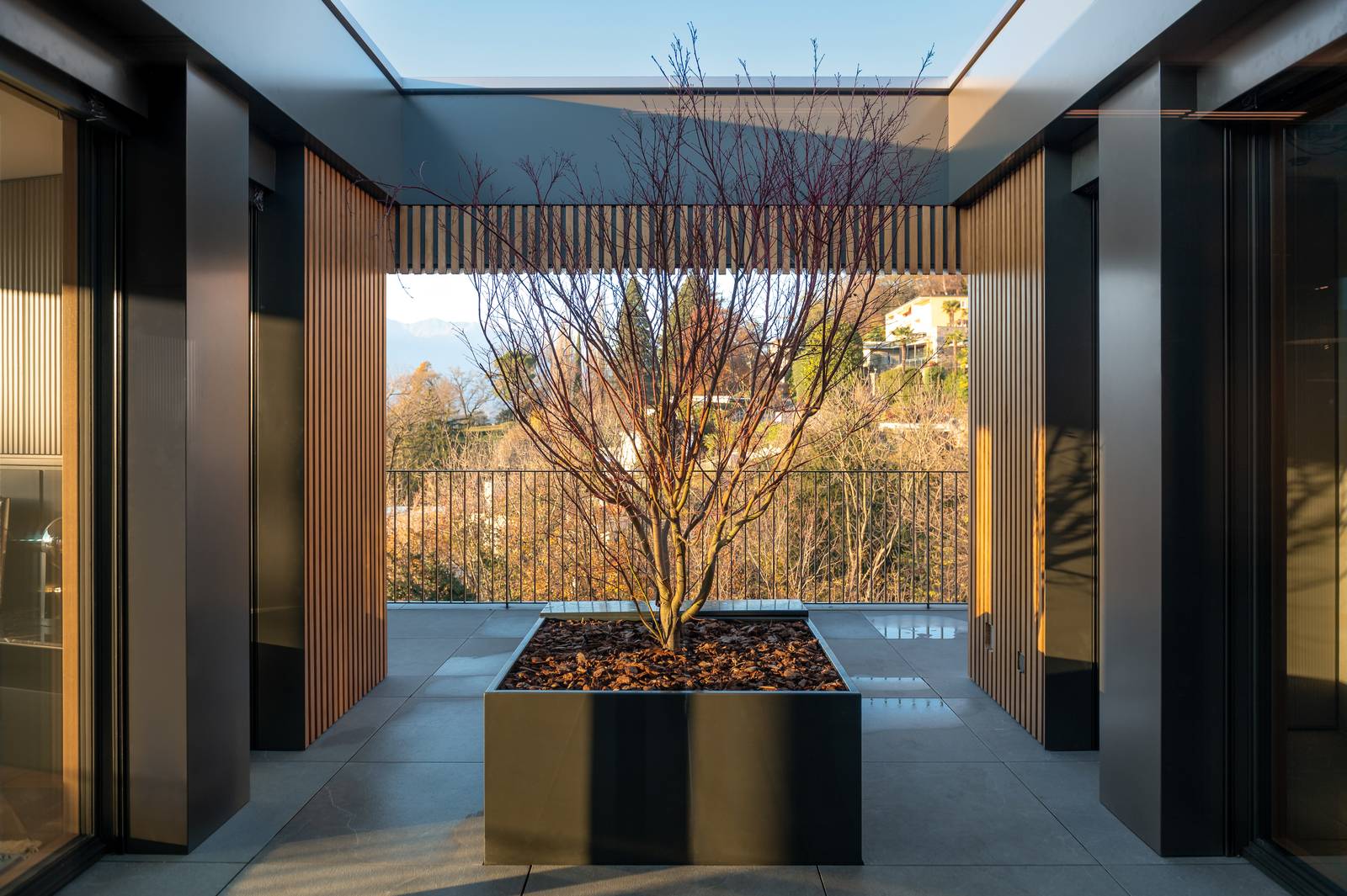 La corte interna a cielo aperto con un albero in una fioriera, un elemento architettonico che porta la natura all'interno della villa. La pavimentazione esterna è realizzata con Lithos Desert 20 mm, finitura bocciardata. La corte interna a cielo aperto con un albero in una fioriera, un elemento architettonico che porta la natura all'interno della villa. La pavimentazione esterna è realizzata con Lithos Desert 20 mm, finitura bocciardata.