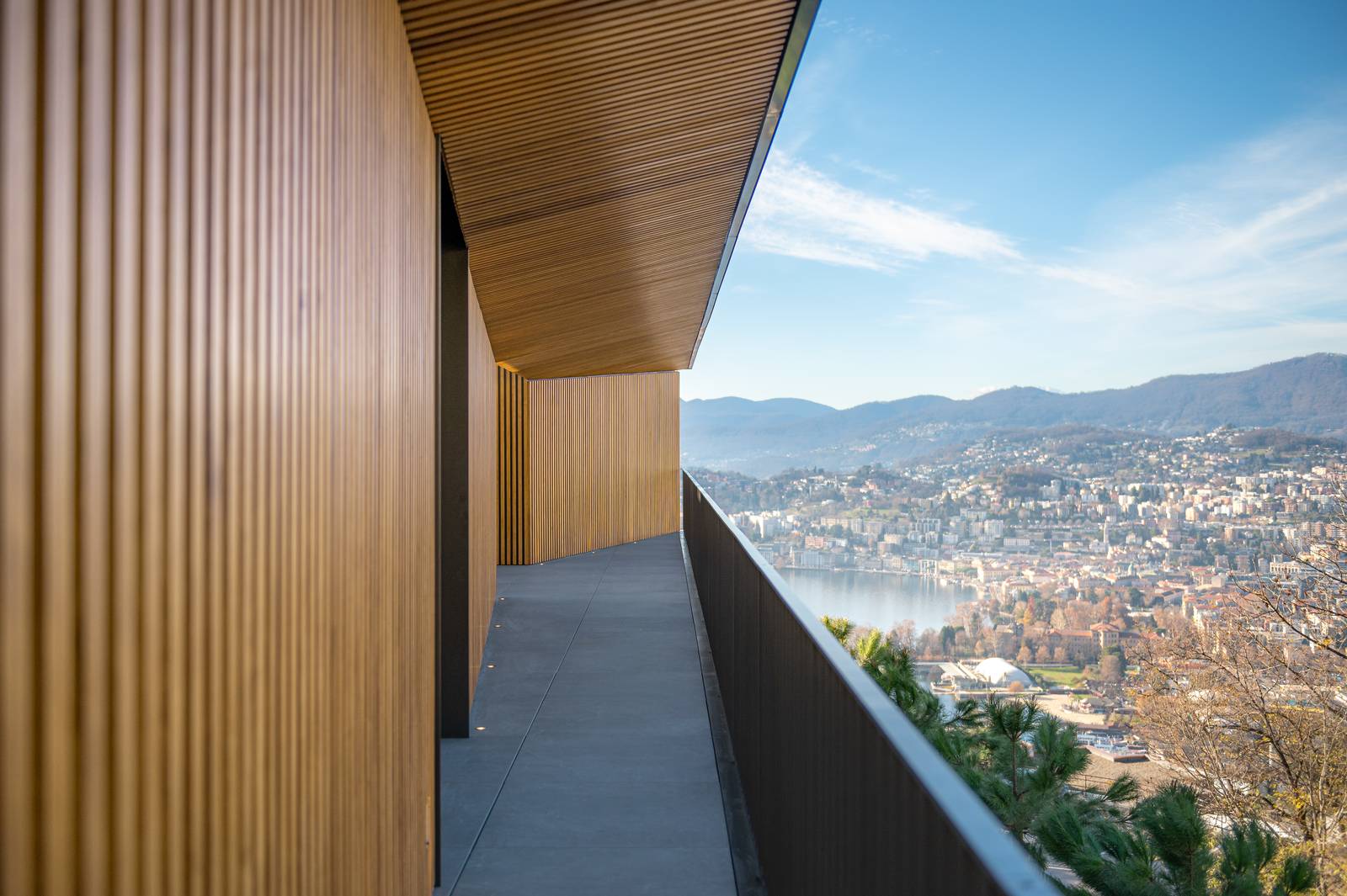 Un balcone come un corridoio esterno della villa, caratterizzato in verticale da rivestimenti a doghe in legno e una ringhiera minimalista, offre una vista spettacolare. La pavimentazione è in Lithos Desert 20 mm. Un balcone come un corridoio esterno della villa, caratterizzato in verticale da rivestimenti a doghe in legno e una ringhiera minimalista, offre una vista spettacolare. La pavimentazione è in Lithos Desert 20 mm.