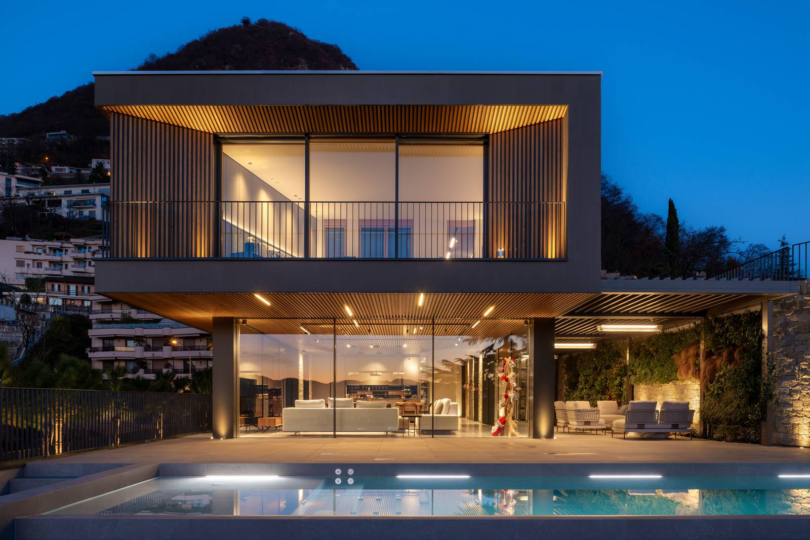 La villa al crepuscolo, con le luci interne ed esterne accese, che ne esaltano l'architettura contemporanea. La piscina riflette la luce, e la continuità visiva tra gli ambienti interni ed esterni è ancora più evidente.. La villa al crepuscolo, con le luci interne ed esterne accese, che ne esaltano l'architettura contemporanea. La piscina riflette la luce, e la continuità visiva tra gli ambienti interni ed esterni è ancora più evidente..