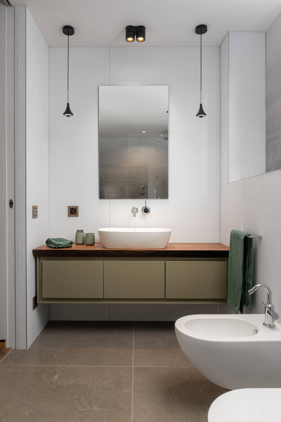 Vista completa del bagno, con il mobile lavabo, lo specchio e il bidet. La parete decorativa in Wonderwall di Cotto d'Este (Kerlite 3,5 mm) è il punto focale, dimostrando come questo materiale trasformi la superficie in un elemento di design anche in una finitura neutra bianca. Vista completa del bagno, con il mobile lavabo, lo specchio e il bidet. La parete decorativa in Wonderwall di Cotto d'Este (Kerlite 3,5 mm) è il punto focale, dimostrando come questo materiale trasformi la superficie in un elemento di design anche in una finitura neutra bianca.