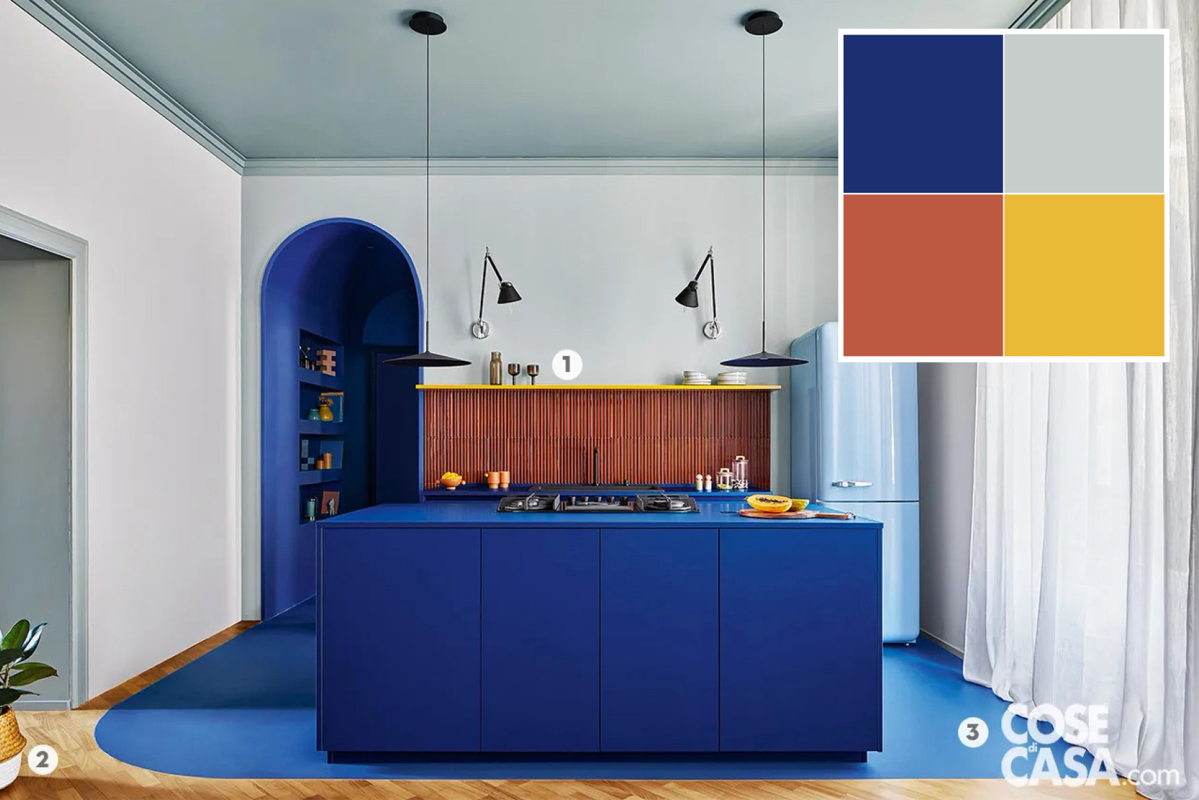 Questa cucina a vista è costituita da due basi, con piano di lavoro dello stesso materiale e colore. Una base, posta lungo la parete, ospita la zona lavaggio e una parte della dispensa ed è completata da una alzatina in piastrelle a rilievo smaltate lucide color terracotta e una mensola gialla. L'altra base, che forma l'isola centrale, include i fornelli e dei contenitori. Posto a fianco e separato dalla composizione, vi è un frigorifero freestanding in stile rétro di colore azzurro. La zona dedicata alla cucina, identificata anche dalla pavimentazione blu realizzata in materiale cementizio, per le sue caratteristiche è di fatto il cuore del living.
Progetto d'interior chromastudio, Via L. Devoto 10, Milano http://www.chromastudio.it @ chromastudio_lab - Foto Riccardo Gasperoni - Styling Elga Ancona + chromastudio - Styling Assistant Samuele Capra e Federica Castaldi