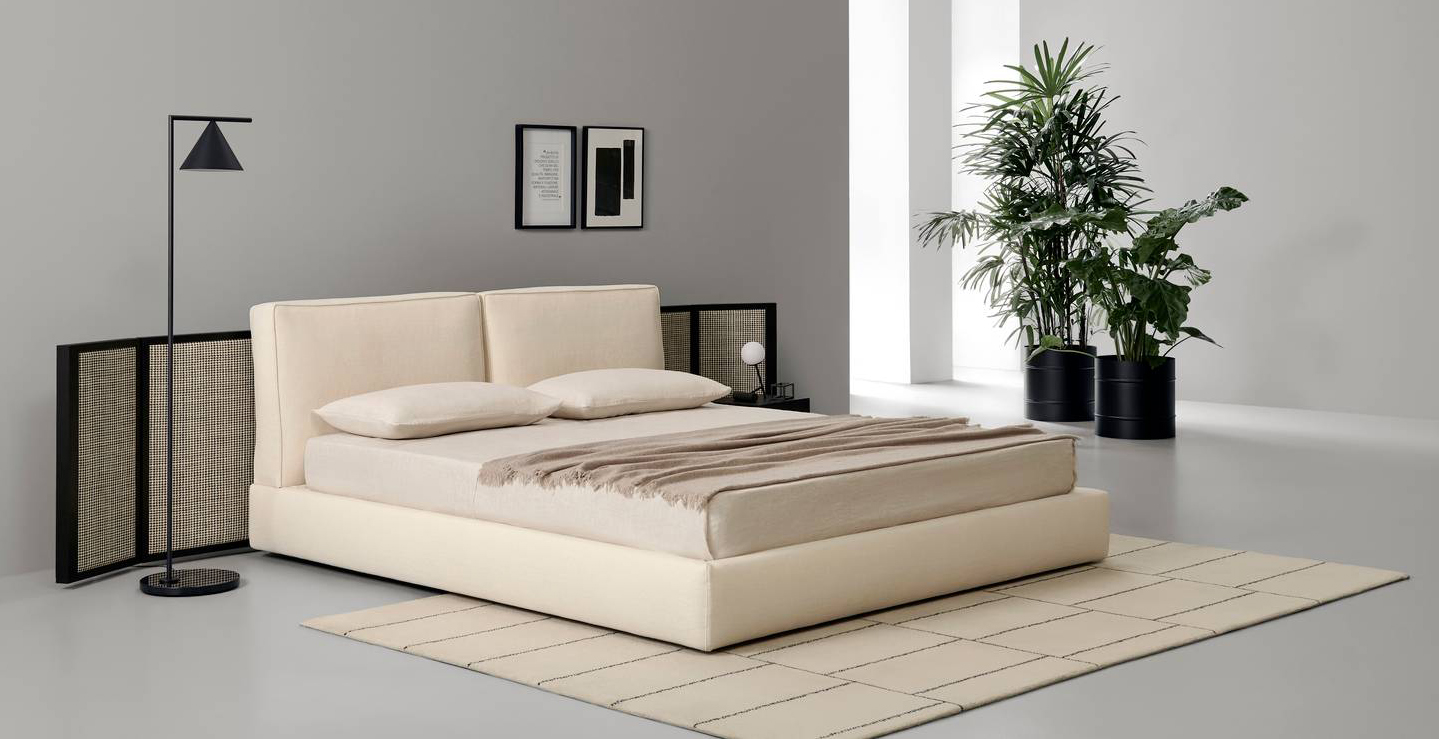 Una forma compatta e spigoli arrotondati per il letto tessile Byron di Porro che è composto da un giroletto imbottito e da una testata con soffici cuscini, entrambi rivestiti in tessuto chiaro. Misura L 178/198 x P 230 x H 89 cm. Prezzo a partire da 3.410 euro + IVA (escluso il paravento in paglia intrecciata). https://www.porro.com/it