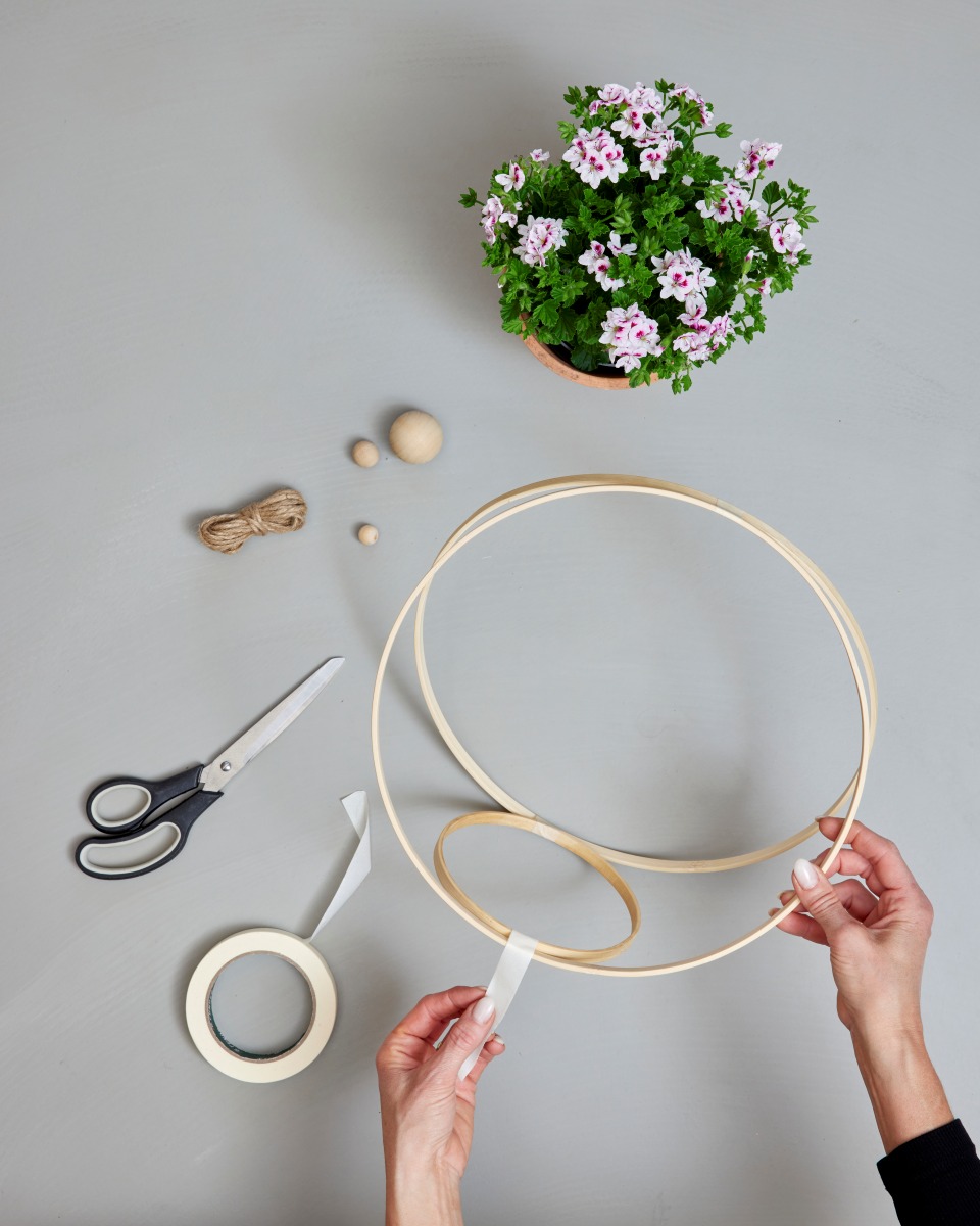 Ad essere utilizzati saranno gli anelli interni dei cerchi da ricamo, che dovranno essere assemblati in una solida struttura tridimensionale. I due cerchi più grandi andranno fissati tra di loro con del nastro adesivo, per poi inserirvi l'anello più piccolo, che fungerà da supporto per il vaso. Copyright immagine Pelargonium for Europe