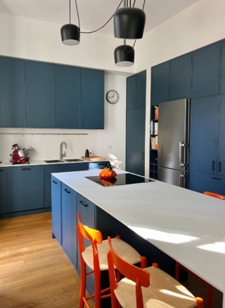 Una cucina dominata dal colore: il blu saturo delle basi e dell’isola è l’assoluto protagonista dello spazio. La finitura opaca esalta la profondità del tono, mentre il piano bianco in HPL crea un contrasto netto e luminoso. Gli sgabelli arancioni introducono un controcanto cromatico vibrante, che accentua la personalità del progetto.