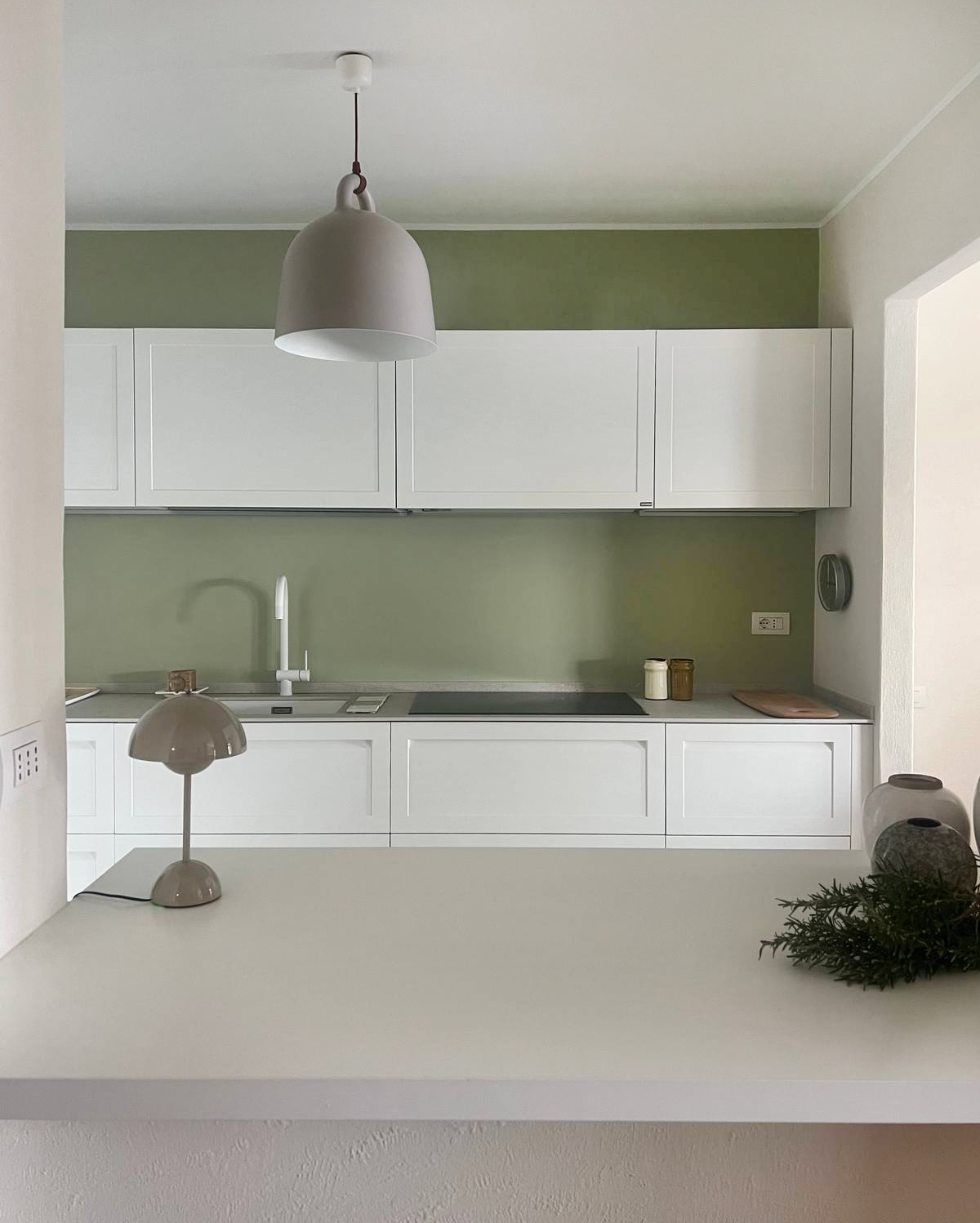 In questa cucina di una casa al lago la parete di fondo è stata dipinta con un verde salvia intenso che crea un contrasto netto con i mobili, che invece sono stati scelti nel colore più neutrale possibile: il bianco. Ecco un’idea semplicissima ma di grande resa. Più il colore è strong e scuro, più lo stacco sarà totale. In questo caso il verde salvia e il bianco creano un contrasto lieve e riposante, seppure di impatto. I pensili, volutamente interrotti prima del soffitto, accentuano la cesura cromatica e sottolineano la relazione tra i due piani di colore.
