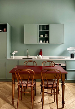 Una scelta progettuale netta e contemporanea: parete e mobili sono trattati con lo stesso tono di azzurro-verde profondo, generando un effetto “a scatola” o Color Block, di grande impatto visivo. L’uniformità cromatica avvolge lo spazio e lo rende coerente e immersivo, mentre la disposizione dei pensili – centrati sulla parete e non a tutta larghezza – introduce un delicato gioco di pieni e vuoti che aggiunge dinamismo e profondità.