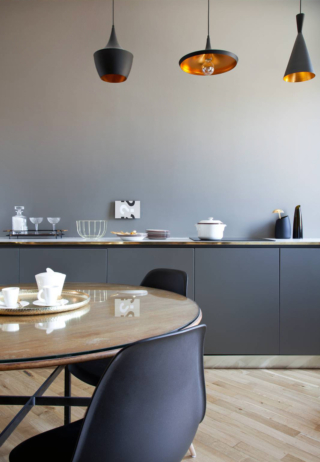 In questo progetto la ricerca dell’armonia tonale sostituisce il contrasto. La parete tortora, avvolgente e delicata, è abbinata a mobili laccati nella stessa gamma cromatica ma di tre tonalità più scure, creando un effetto degradé discreto e sofisticato. L’assenza di pensili e mensole contribuisce a un’estetica essenziale, quasi da consolle, coerente con la collocazione della cucina nella zona pranzo. Le tre sospensioni puntuali sopra il piano lavoro evocano un’atmosfera più domestica e rilassata, ibridando la funzione tecnica con il linguaggio del living.