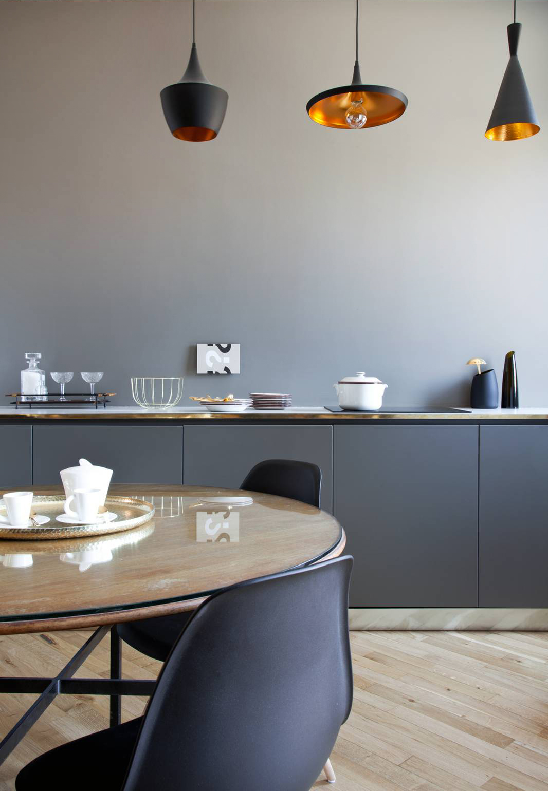 In questo progetto la ricerca dell’armonia tonale sostituisce il contrasto. La parete tortora, avvolgente e delicata, è abbinata a mobili laccati nella stessa gamma cromatica ma di tre tonalità più scure, creando un effetto degradé discreto e sofisticato. L’assenza di pensili e mensole contribuisce a un’estetica essenziale, quasi da consolle, coerente con la collocazione della cucina nella zona pranzo. Le tre sospensioni puntuali sopra il piano lavoro evocano un’atmosfera più domestica e rilassata, ibridando la funzione tecnica con il linguaggio del living.