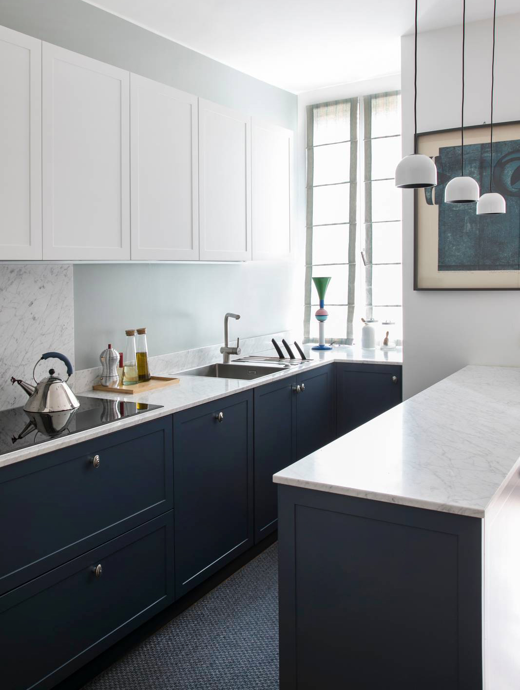 Un progetto che dimostra come la dissonanza cromatica possa generare armonia. Le basi blu notte, quasi nere, dialogano con pensili bianchi dalle cornici sottili e con una parete verde pastello chiaro. L’insieme nasce dal desiderio di valorizzare un colore intenso senza appesantire lo spazio, calibrando le masse visive e i contrasti. Il risultato è una composizione equilibrata e raffinata, dove ogni elemento contribuisce a un racconto cromatico coerente.
Questa scelta è stata dettata da diverse esigenze: il colore blu scuro era la passione della padrona di casa e non ci voleva rinunciare, ma i pensili in una tinta così scura sarebbero stati troppo invasivi. Infine, senza un colore sulla parete sembrava che mancasse qualcosa. 