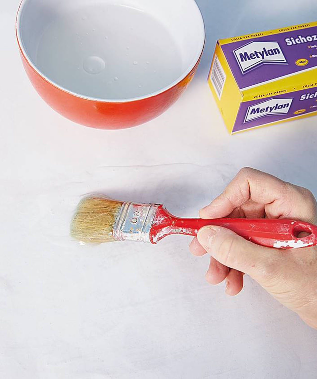 Preparare la colla seguendo le istruzioni sulla confezione. Una volta pronta, appoggiare il primo foglio su una superficie protetta, e stendere la colla sul retro. Muovere il pennello in orizzontale distribuendo la colla in modo uniforme. Preparare la colla seguendo le istruzioni sulla confezione. Una volta pronta, appoggiare il primo foglio su una superficie protetta, e stendere la colla sul retro. Muovere il pennello in orizzontale distribuendo la colla in modo uniforme.