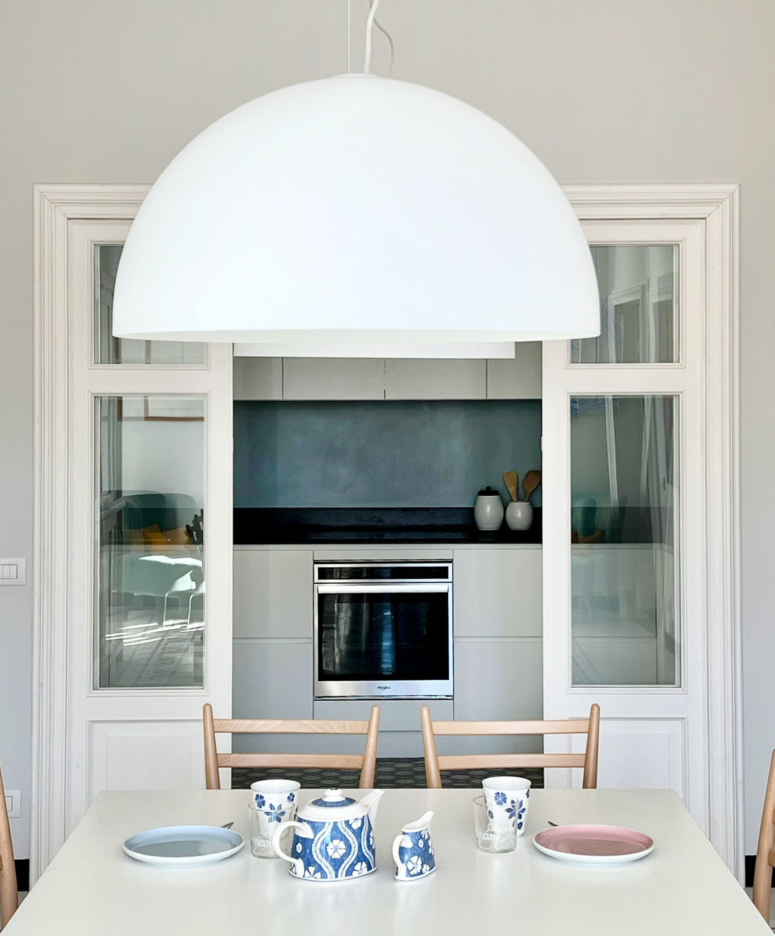 Vetrata semplice -  In questo soggiorno la zona dedicata alla cucina si trova in una posizione senza la finestra e prende luce da una vetrata in legno bianco alta 240 centimetri e larga 2 metri che la connette alla zona del pranzo. Il suo disegno è molto semplice, ma le cornici lavorate la rendono elegante e raffinata. La perfetta centratura e la simmetria sulla parete creano una composizione bilanciata pur nella sua semplicità. Vetrata semplice -  In questo soggiorno la zona dedicata alla cucina si trova in una posizione senza la finestra e prende luce da una vetrata in legno bianco alta 240 centimetri e larga 2 metri che la connette alla zona del pranzo. Il suo disegno è molto semplice, ma le cornici lavorate la rendono elegante e raffinata. La perfetta centratura e la simmetria sulla parete creano una composizione bilanciata pur nella sua semplicità.