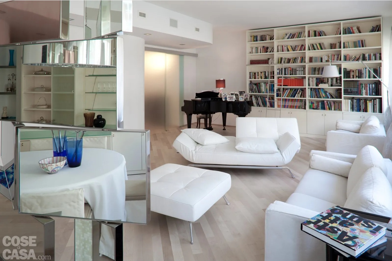 Nell’angolo conversazione gli imbottiti gemelli in tessuto di B&B sono abbinati a divano e pouf in pelle, con lavorazione capitonné, della serie Smala di Ligne Roset. Nell’angolo, la lampada da terra con stelo orientabile è il modello Tolomeo di Artemide. A parete, una struttura modulare in laccato avorio, realizzata su disegno, sfrutta l’altezza del soffitto.