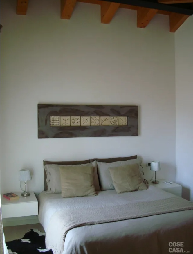 Toni chiari per la camera da letto matrimoniale in mansarda. Il letto, posizionato quasi in nicchia, ha una testiera volutamente ridotta nell’ingombro ed è servito da due bianchi comodini sospesi, che alleggeriscono l’insieme e sostengono due piccole abat-jour dal gusto vagamente retrò. Minimali anche le finiture: rovere sbiancato a pavimento e pareti bianco-avorio, che rendono più sofisticata la biancheria e i cuscini declinati nei toni dell’écru.