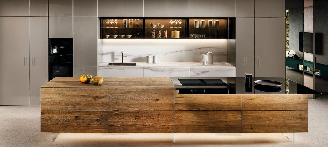 Le ante delle basi dell'isola della cucina 36e8 Cut di LAGO sono caratterizzate da un'apertura a gola che non interrompe l'uniformità della superficie in legno con venature a vista. A parete trovano posto le basi nella finitura marmo con la zona lavaggio, le colonne e i pensili a sviluppo orizzontale in vetro fumé. Prezzo su richiesta. https://www.lago.it