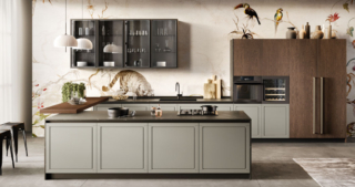 Spiccano sulla tappezzeria fantasia i pensili con le ante in vetro fumé, illuminati da profili LED interni, nella cucina Myriad 1 di Moretti Compact Cucine che è caratterizzata da un'imponente isola centrale collegata agli elementi lineari dal massiccio piano snack, impiallacciato Rovere Moka come le colonne, in appoggio sul piano. Le basi hanno le ante senza maniglia in Laccato Pietra Opaco. Un modulo base da 60 cm, prezzo 242 euro (esclusi top, gola/maniglia e zoccolo). https://cucine.moretticompact.it