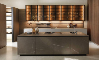 Nella cucina Telero di Euromobil si articola intorno all'isola con le basi in gres Laminam In-Side pietra piasentina taupé e attrezzata con il lavello e il piano induzione. Sulla parete di fondo sono appesi i pensili Teca con il telaio testa di moro e vetro fumé con una struttura in olmo Michelangelo come la boiserie attrezzata Horizon e le colonne Antis. Il pensile Teca misura L 45 x  H 120 cm, prezzo 856 euro + IVA. https://www.euromobil.com