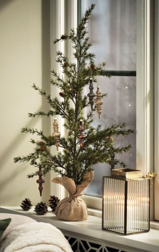 Ha un aspetto naturale l'abete Fenrir di Jysk che è caratterizzato dalla presenza di piccole pigne e di un basamento ricoperto da juta. Per decorarlo sono stati appesi una serie di addobbi allungati Lucia nelle tonalità del marrone con un risultato superchic. Misura Ø 35 x H 90 cm. Prezzo 36,95 euro. https://jysk.it