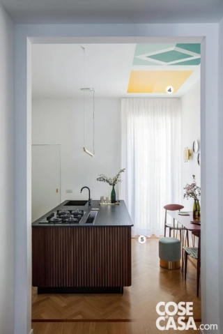 In questa cucina l'isola centrale, che ha un piano in marmo nero e che ospita le funzioni operative, quali lavello e piano cottura, è rivestita da listelli di legno in tinta mogano, che richiamano la cornice del pavimento in parquet a spina di pesce. Il mobile è circondato da vari elementi colorati, che risultano nell'insieme molto delicati, quali il color amaranto del piano del tavolo, il pouf azzurro, il rivestimento decor del soffitto giallo e verde menta: l'insieme risulta davvero equilibrato e raffinato.
Progetto arch. Elena Cerizza, Milano, Tel. 02/36751450 http://www.elenacerizza.it - Foto Cristina Galliena Bohman - Styling Laura Mauceri