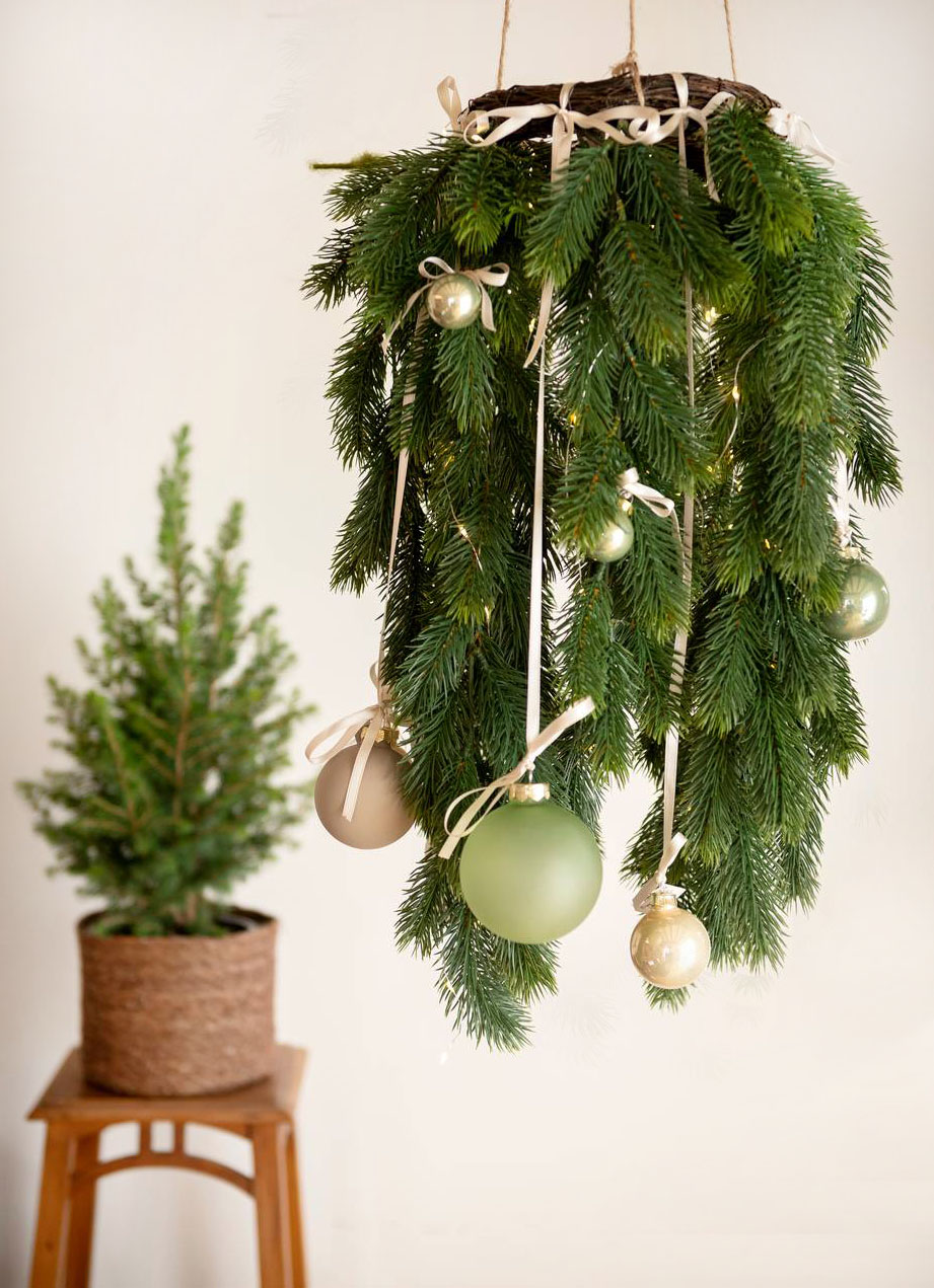 Una corona di pino cadente in materiale sintetico PE, appesa al soffitto, può essere una valida alternativa all'abete tradizionale. Misura Ø 110 cm. Prezzo 29,90 euro. È decorata con palline, grandi e piccole, nelle delicate tonalità verde e beige, sospese per mezzo di nastrini colorati. Tutto in vendita nei Viridea Garden Center. https://shop.viridea.it