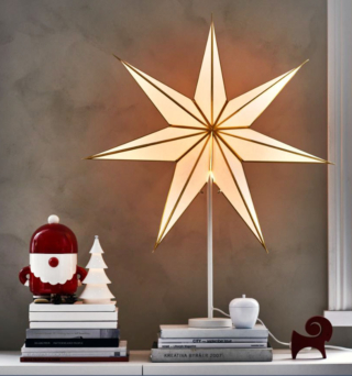 Fa parte della composizione natalizia di Ikea Italia il barattolo con coperchio con la forma di Babbo Natale sugli sci in legno chiaro della collezione Vinterfint: è prodotto in terraglia colorata con una forma stilizzata. Misura Ø 13 x H 24 cm. Prezzo 15 euro. Accanto è posizionata la lampada con il paralume Strala a forma di stella con dettagli in metallo color oro. Misura Ø 70 cm. Prezzo 4,95 euro. La base bianca per la lampada, misura Ø 12 x H 48 cm e costa 7 euro. https://www.ikea.com