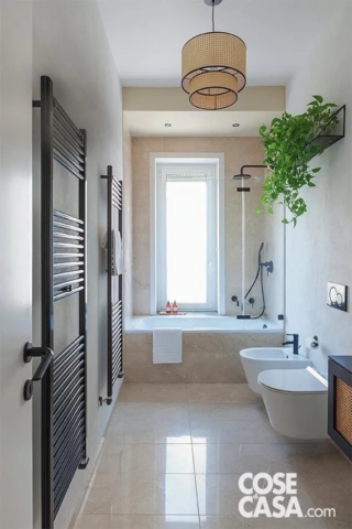 In questo bagno si è optato per un rivestimento in marmo, che con la sua finitura lucida esalta la luce naturale presente per via della grande finestra centrale posta sul lato corto sopra la vasca.
Il lampadario centrale è in paglia di Vienna con struttura nera: i suoi colori richiamano quelli prevalenti nella stanza, ossia il beige del pavimento in marmo e delle pareti in cementine e resina, e il nero della rubinetteria e degli scaldasalviette, e si coordina perfettamente con il mobile del lavabo realizzato su disegno negli stessi colori e materiali. L'insieme risulta equilibrato unendo uno stile minimal e contemporaneo, dato dalle linee essenziali e dai dettagli neri, e un tocco di classicità e di naturalità per l'uso della paglia di Vienna per lampadario e mobile.
Progetto Mariana Martini e Fanni Szarvas-Mariana Martini Studio, Milano, Tel. 02/97802034 - http://www.marianamartini.it . Foto Cristina Galliena Bohman - Styling Francesca Martinez