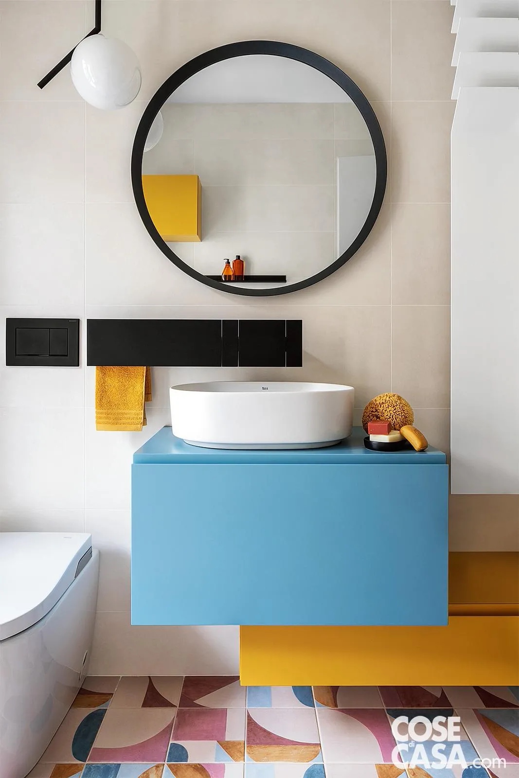 Questo bagno presenta uno stile molto giovane e allegro grazie alla presenza di svariati elementi colorati, quali i disegni multicolor delle piastrelle del pavimento, il senape e l'azzurro dei pensili sotto il lavabo, il tono delicato delle piastrelle a parete. Qui si inserisce bene la lampada a sospensione dalle linee semplici, costituita da un globo in vetro soffiato opaco e una struttura in metallo nero, che si abbina agli altri elementi neri che spiccano, ossia la rubinetteria, il porta asciugamani, la cornice dello specchio: il risultato è equilibrato e di grande gusto.
Progetto e styling arch. Martina Chiara Maria Pozzi, email martina_pozzi_17@hotmail.com, Tel. 327/1267024, IG mp_archistudio - Foto Riccardo Gasperoni