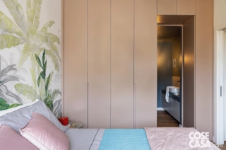 L'armadio con ante in laccato opaco scelto per questa camera ha una struttura a ponte che incornicia la porta di accesso al bagno a uso esclusivo e presenta un originale colore rosa pastello. Tutta la stanza è giocata su colori soft, con copriletto, cuscini e plaid in rosa e azzurro, e con una carta da parati a motivo jungle, che riveste la parete posteriore del letto e che vede la prevalenza del verde in varie sfumature: il risultato è un insieme rilassante e delicato per la zona dedicata al riposo.
Progetto: Alba Studio, arch. Francesca Albertario, Milano, Tel. 02/94380177 https://www.alba-studio.com IG: @f_albertario - Foto: Cristina Galliena Bohman - Styling: Laura Mauceri