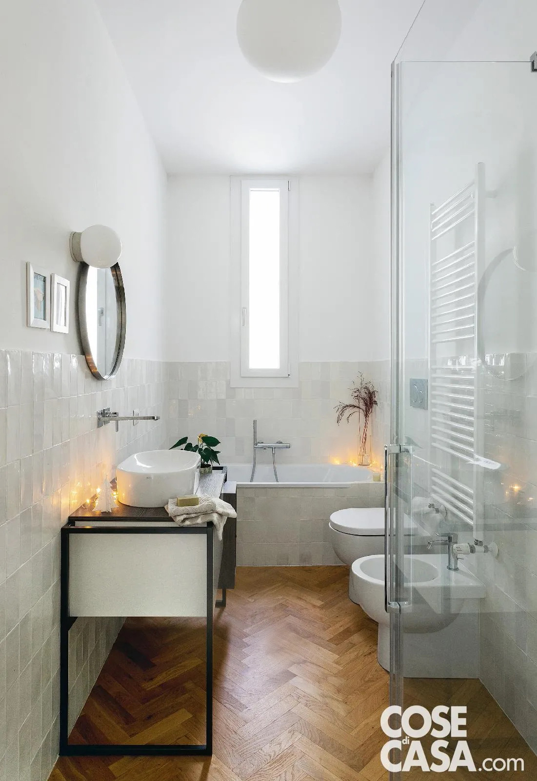 In questo bagno è stato scelto un lampadario a sospensione di forma sferica molto grande, in vetro opaco di colore bianco, che va ad accentuare il senso di luminosità dell'ambiente. Il locale infatti è molto luminoso grazie a una finestra verticale centrale e anche grazie alla prevalenza del bianco delle piastrelle lucide del rivestimento, di mobili, infissi e sanitari. Unica nota scura è il parquet a spina di pesce in rovere, che crea un bel contrasto con il resto e accentua l'eleganza del bagno.
Progetto: arch. Nicola Carnevali - Foto: Studio Roy - Styling: Lidia Elisa Covello
