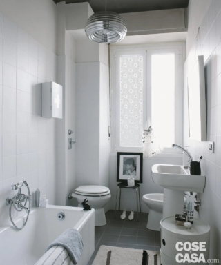 Questo bagno presenta dei sanitari dalle linee classiche ed è caratterizzato dalla luminosità e dalla preponderanza del bianco, usato per sanitari, infissi, piastrelle di rivestimento e mobiletto cilindrico. Un ambiente semplice ed essenziale, in cui spicca il lampadario realizzato in alluminio lucidato che dona un tocco di modernità.
Styling: Cristina Nava - Foto: Denise Bonenti