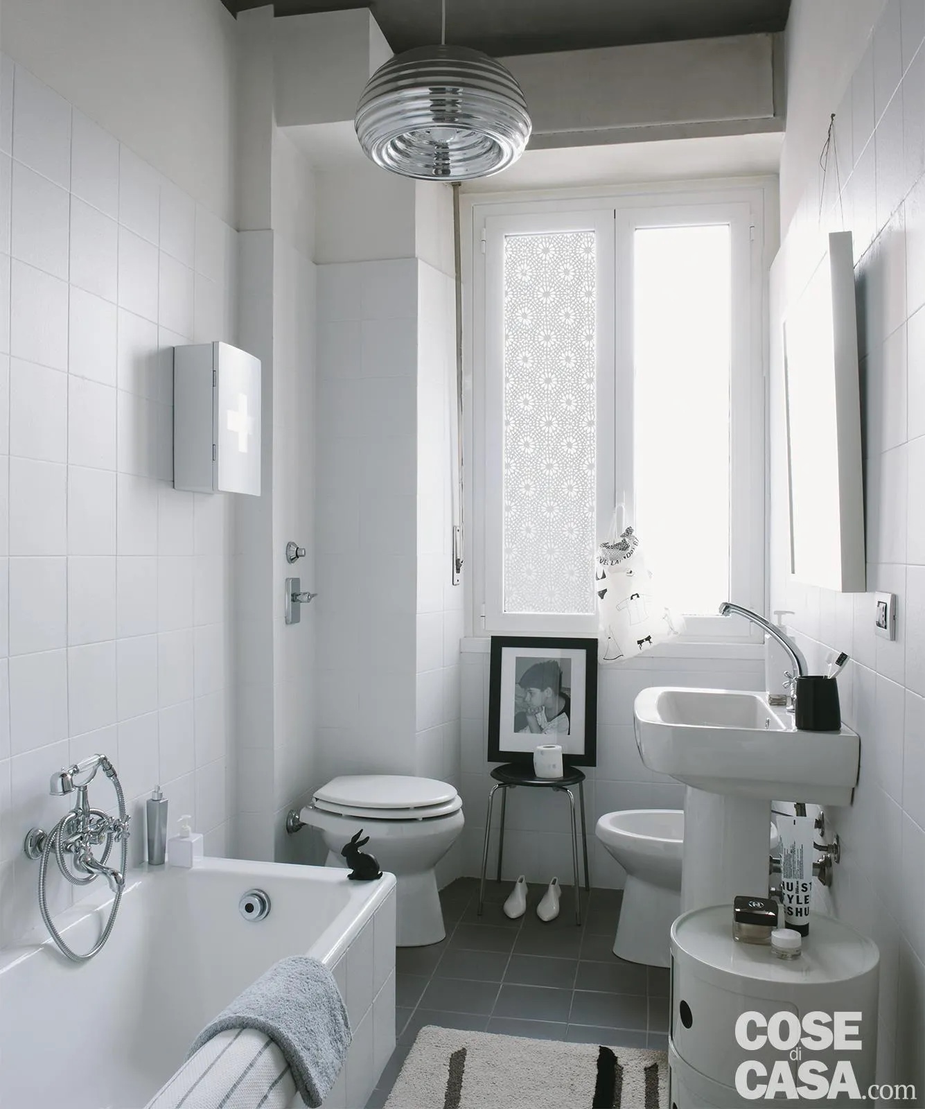 Questo bagno presenta dei sanitari dalle linee classiche ed è caratterizzato dalla luminosità e dalla preponderanza del bianco, usato per sanitari, infissi, piastrelle di rivestimento e mobiletto cilindrico. Un ambiente semplice ed essenziale, in cui spicca il lampadario realizzato in alluminio lucidato che dona un tocco di modernità.
Styling: Cristina Nava - Foto: Denise Bonenti