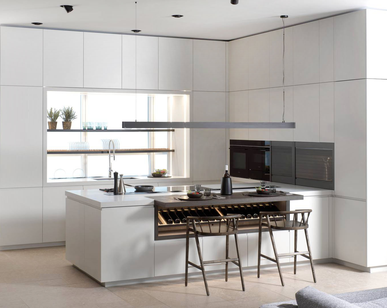 La grande penisola attrezzata con gli espositori per bottiglie sotto il piano snack domina la cucina E4.70 di Porcelanosa che si apre completamente sul living. Le ante sono nella finitura porcellana opaca bianca e il piano di lavoro è realizzato in composito minerale Krion Light Grey. Gli interni sono in rovere Cuero Soft. Prezzo su richiesta. https://www.porcelanosa.com