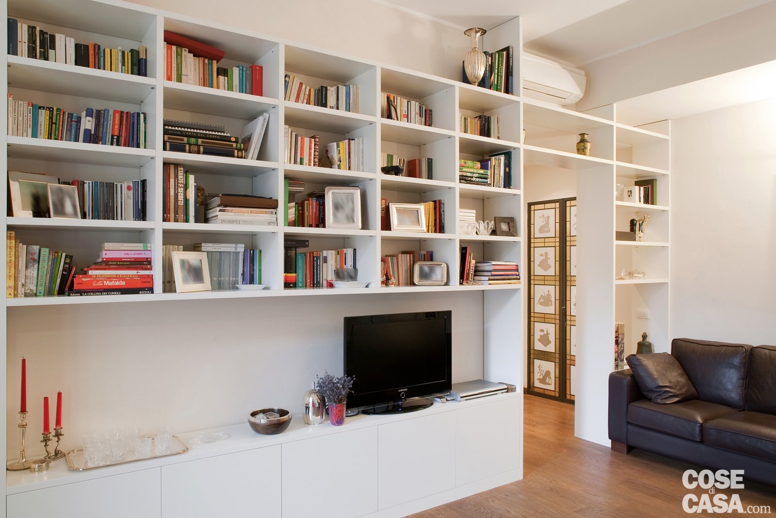 Una libreria a tutta altezza, che separa il living da ingresso e cucina, costituita da vani a giorno dalla struttura regolare, che occupa lo spazio sulla porta, sopra la quale è collocato il climatizzare e si estende fino a terra sul lato destro. A sinistra, invece, la parte inferiore è occupata da basi che ospitano il televisore ed elementi decorativi. Progetto: arch. Alessandra Sacchi; Foto di Cristina Fiorentini. Una libreria a tutta altezza, che separa il living da ingresso e cucina, costituita da vani a giorno dalla struttura regolare, che occupa lo spazio sulla porta, sopra la quale è collocato il climatizzare e si estende fino a terra sul lato destro. A sinistra, invece, la parte inferiore è occupata da basi che ospitano il televisore ed elementi decorativi. Progetto: arch. Alessandra Sacchi; Foto di Cristina Fiorentini.