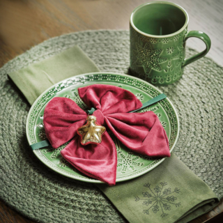 Una raffinata sfumatura verde oliva per il posto tavola per le feste di Jysk che è composto dal  piatto Malakit in porcellana lucida con un motivo naif di stelle e fiocchi di neve, dalla tazza coordinata e dalla tovaglietta rotonda Flinsten in iuta verde con un aspetto rustico. Il piatto misura Ø 20 cm, prezzo 5,50 euro. La tazza misura Ø 8 x H 9 cm, prezzo 4 euro. La tovaglietta misura Ø 38 cm, prezzo 5 euro. Il grande fiocco in velluto rosso con la stellina dorata funge da segnaposto. https://jysk.it