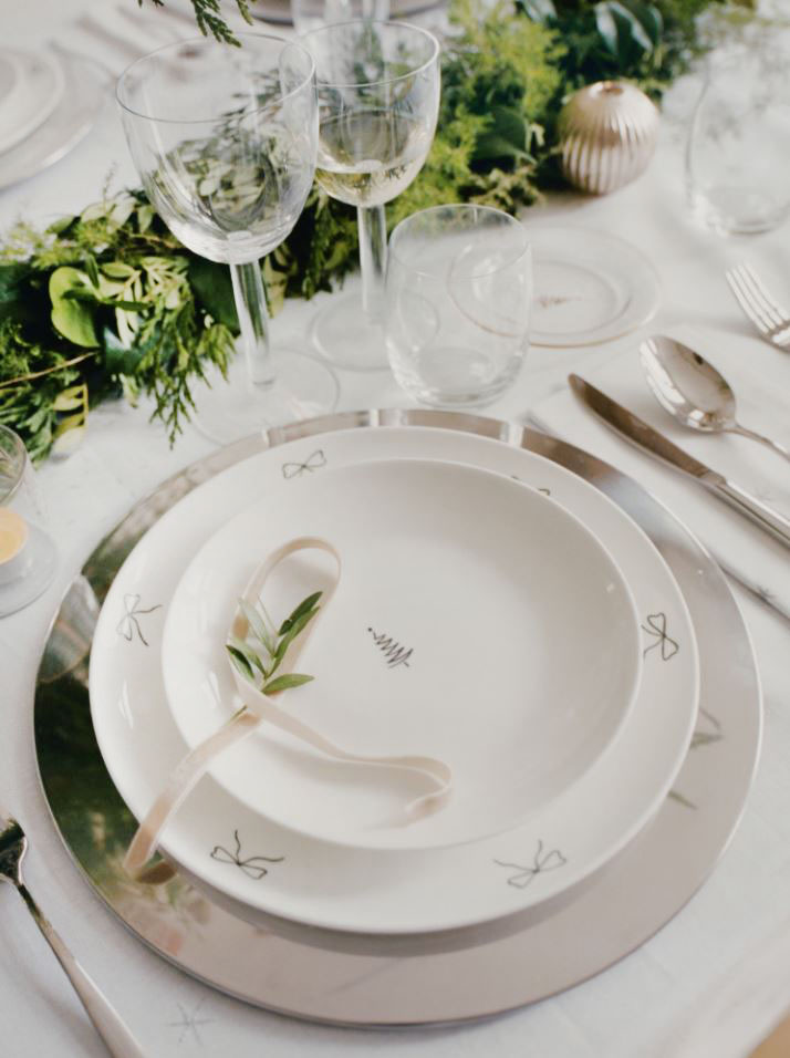 Sottili decori grafici neri per i piatti in porcellana bianca che compongono il posto tavola natalizio   di Mango Home che è completato dal sottopiatto argentato e dalle posate in acciaio. Il piatto piano è dipinto a mano e decorato da piccoli fiocchi neri lungo il bordo, misura Ø 26,5 cm, prezzo 12,99 euro. Il piatto dessert decorato da un abete stilizzato al centro misura Ø 21 cm, prezzo 8,99 euro. https://shop.mango.com