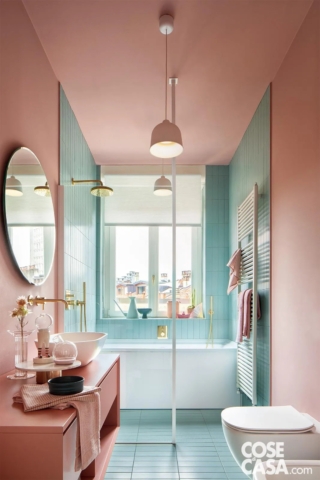 In questo bagno, lungo e molto luminoso per via della grande finestra sul fondo, il verde acqua delle piastrelle strette e verticali ricopre a tutta altezza la parte finale dell'ambiente, che ospita la vasca ed è separato da un divisorio in vetro trasparente. La parte iniziale del bagno con i sanitari è invece dipinta di rosa, come l'intero soffitto e il mobile con il lavabo.
Si tratta di un bagno dalle tonalità fresche e divertenti che infondono vivacità e allegria.
Progetto: Studio Tenca & Associati, arch. Emilio Tenca Milano, Tel. 02/3319239 - https://www.studiotenca.it - Foto: Riccardo Gasperoni - Styling: Irene Baratto