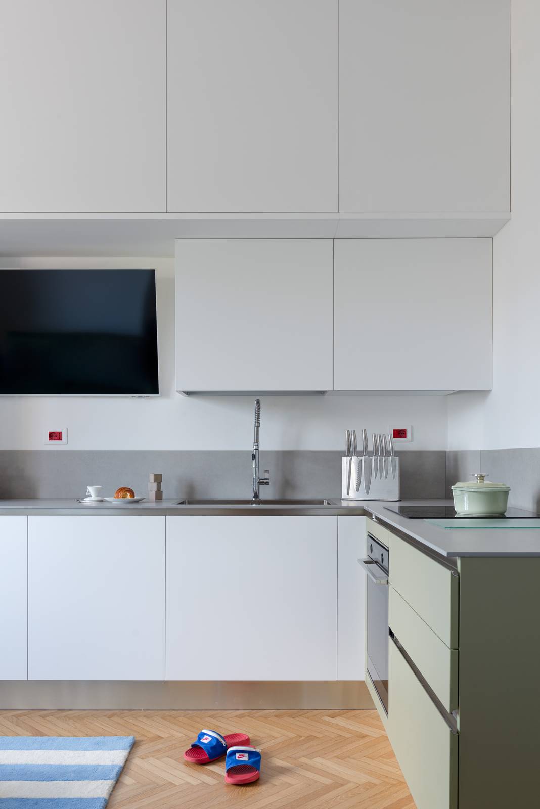 Cucina con pensili e basi laccati bianco opaco con piano e alzatina in ceramica. A destra basi con frontali verde salvia. Pavimento in parquet a spina di pesce. Cucina con pensili e basi laccati bianco opaco con piano e alzatina in ceramica. A destra basi con frontali verde salvia. Pavimento in parquet a spina di pesce.