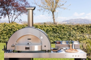 Con il forno per outdoor Classico 4 Pizze di Alfa Forni si possono preparare più pizze contemporaneamente. L’ampia camera di cottura consente di sfornare fino a 4 pizze in circa 90 secondi e cuocere anche pane, con una capacità di infornata fino a 4 kg di pane, e altri piatti, come arrosti e focacce. Grazie alla volta in acciaio inox e alla coibentazione in fibra ceramica, il forno raggiunge rapidamente la temperatura di esercizio — fino a 500 °C in circa 30 minuti — e mantiene il calore in modo stabile. Ha finitura in ardesia grigia. Con il Kit Hybrid opzionale è possibile trasformare il modello in una versione ibrida per cuocere anche a legna. Pesa 118 kg e misura L 114 x P 72,5 x H 101 cm. Prezzo, Iva esclusa, della versione a gas 3.360 euro; prezzo, Iva esclusa, della base con ruote 650 euro. www.alfaforni.com