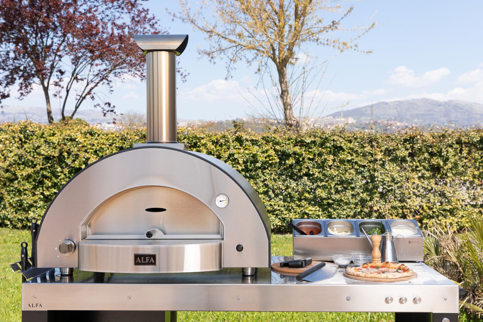 Con il forno per outdoor Classico 4 Pizze di Alfa Forni si possono preparare più pizze contemporaneamente. L’ampia camera di cottura consente di sfornare fino a 4 pizze in circa 90 secondi e cuocere anche pane, con una capacità di infornata fino a 4 kg di pane, e altri piatti, come arrosti e focacce. Grazie alla volta in acciaio inox e alla coibentazione in fibra ceramica, il forno raggiunge rapidamente la temperatura di esercizio — fino a 500 °C in circa 30 minuti — e mantiene il calore in modo stabile. Ha finitura in ardesia grigia. Con il Kit Hybrid opzionale è possibile trasformare il modello in una versione ibrida per cuocere anche a legna. Pesa 118 kg e misura L 114 x P 72,5 x H 101 cm. Prezzo, Iva esclusa, della versione a gas 3.360 euro; prezzo, Iva esclusa, della base con ruote 650 euro. www.alfaforni.com