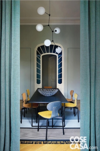 Questa sala da pranzo di un'abitazione dei primi anni del Novecento occupa un locale separato rispetto al resto della zona giorno, nel quale spicca una bellissima porta d'epoca, centinata e in legno laccato, con vetri smerigliati blu in stile Liberty. L'arredamento ne richiama i colori, con varie tonalità del blu e dell'azzurro, nel tappeto, nelle tende e nello schienale delle sedie, ma gioca sul contrasto di stili, per via di un tavolo nero rettangolare di forma moderna, delle sedie in stile nordico e del lampadario di design.
Progetto d'interior: arch. Laura Marchesi Laura Marchesi e Giorgio Osella, tomdesign, c.so San Maurizio 73/b, Torino, Tel. 011/19707397 https://www.tomdesign.it - Foto: Barbara Corsico - Styling: Chiara Dal Canto