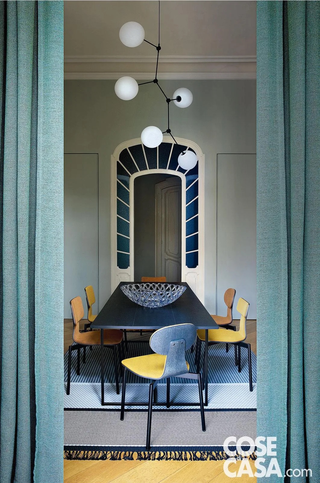 Questa sala da pranzo di un'abitazione dei primi anni del Novecento occupa un locale separato rispetto al resto della zona giorno, nel quale spicca una bellissima porta d'epoca, centinata e in legno laccato, con vetri smerigliati blu in stile Liberty. L'arredamento ne richiama i colori, con varie tonalità del blu e dell'azzurro, nel tappeto, nelle tende e nello schienale delle sedie, ma gioca sul contrasto di stili, per via di un tavolo nero rettangolare di forma moderna, delle sedie in stile nordico e del lampadario di design.
Progetto d'interior: arch. Laura Marchesi Laura Marchesi e Giorgio Osella, tomdesign, c.so San Maurizio 73/b, Torino, Tel. 011/19707397 https://www.tomdesign.it - Foto: Barbara Corsico - Styling: Chiara Dal Canto