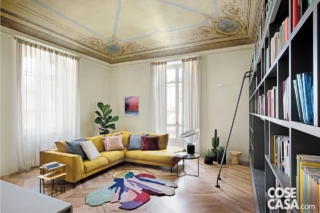 In questa casa di fine Ottocento, la zona giorno possiede un soffitto a volta interamente affrescato che è stato restaurato con cura per riportarlo all'aspetto originario.
I colori prevalenti della pittura, giallo ocra e azzurro carta da zucchero, sono stati ripresi nell'arredamento del soggiorno, in cui sono stati collocati un divano angolare color ocra dallo stile contemporaneo, cuscini azzurri e rosa, un tappeto con tonalità in pendant, una libreria grigia lineare e tavolini e lampade di design.