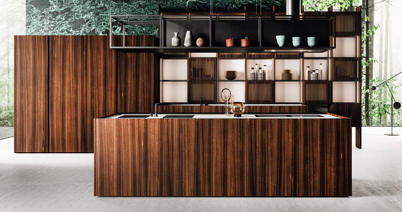Le ante delle basi e delle colonne della cucina Bosco di Rastelli sono impiallacciate in eucalipto. La forma essenziale dell'isola, attrezzata con il piano cottura a induzione e il lavello con rubinetto a scomparsa, mette in evidenza la matericità e la venatura del legno. Prezzo su richiesta. https://rastellidesign.it