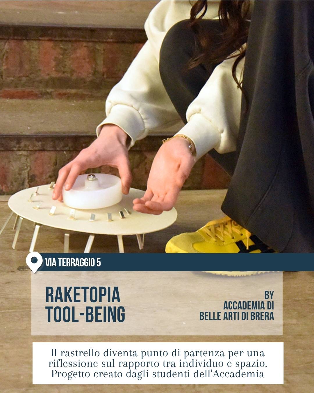 Fuorisalone 2026 Milano, 5VIE Design District: installazione “Raketopia Tool-Being” dell’Accademia di Belle Arti di Brera. Una persona sistema un oggetto circolare bianco simile a un piccolo tavolo-scultura, ispirato al rastrello, seduta sui gradini di uno spazio espositivo.