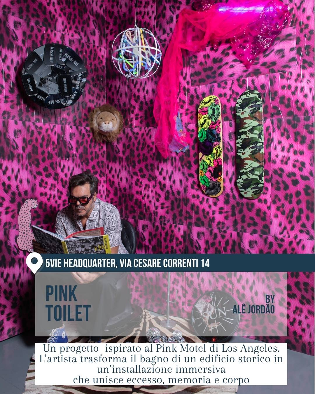 Fuorisalone 2026 Milano, 5VIE Design District: installazione “Pink Toilet” di Alê Jordão. Un uomo seduto legge in un bagno trasformato in ambiente immersivo con pareti rosa leopardate, skateboard decorati e dettagli pop dall’estetica provocatoria.