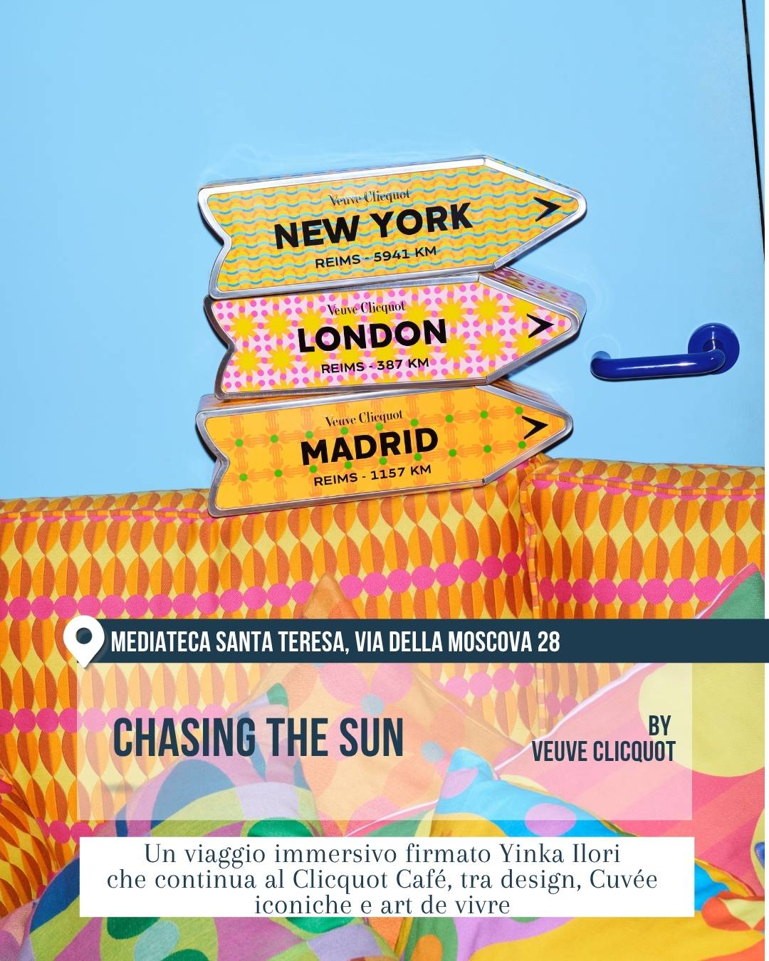 Fuorisalone 2026, Milano Design Week: “Chasing the Sun” alla Mediateca Santa Teresa, via della Moscova 28, by Veuve Clicquot. Interno coloratissimo con divano e cuscini a motivi vivaci, parete azzurra e insegne decorative con le scritte New York, London e Madrid. Installazione immersiva firmata Yinka Ilori tra design, convivialità e art de vivre.